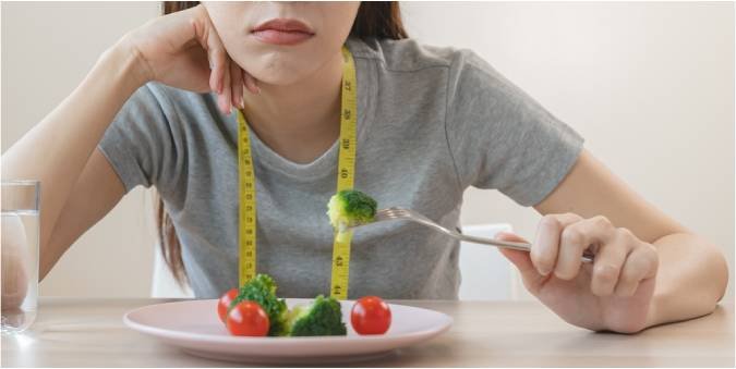 A person eating food while measuring it with a tape measure, symbolizing the mental and emotional struggles associated with eating disorders or unhealthy relationships with food.